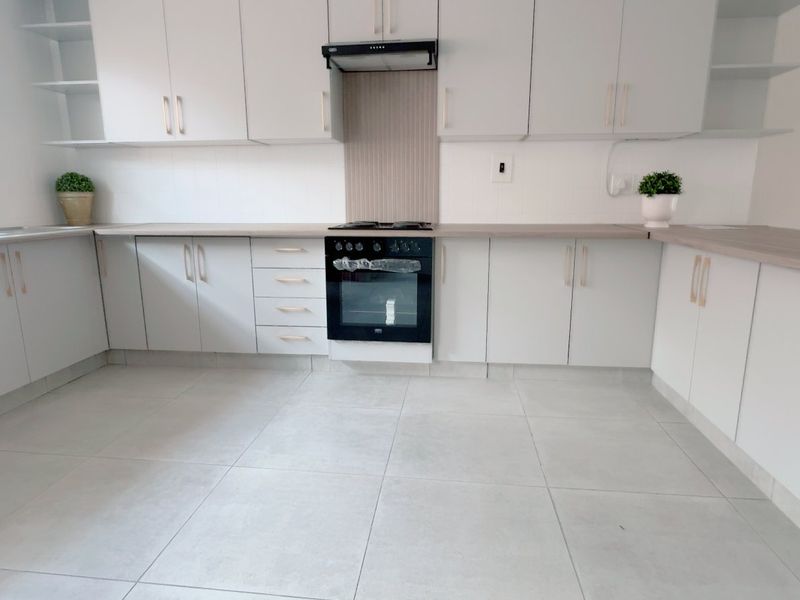 A clean, modern kitchen featuring light-toned cabinetry, laminate countertops, built-in oven with extractor fan, and neutral tiled flooring.