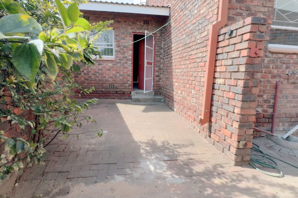 A rear exterior view of the townhouse featuring a paved patio area, face brick walls, and a secure entrance door.