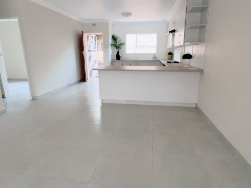 An open-plan living and kitchen area featuring neutral tiled flooring, modern cabinetry, and a breakfast bar, offering a bright and versatile living space.