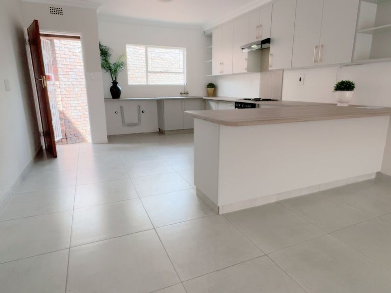 A clean, modern kitchen featuring white cabinetry, light wood-tone countertops, tiled flooring, and an integrated hob with extractor fan.