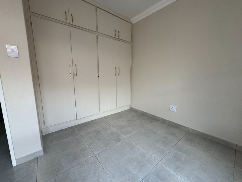 A clean, empty bedroom featuring neutral tiled flooring and ample built-in cupboard storage with classic hardware.