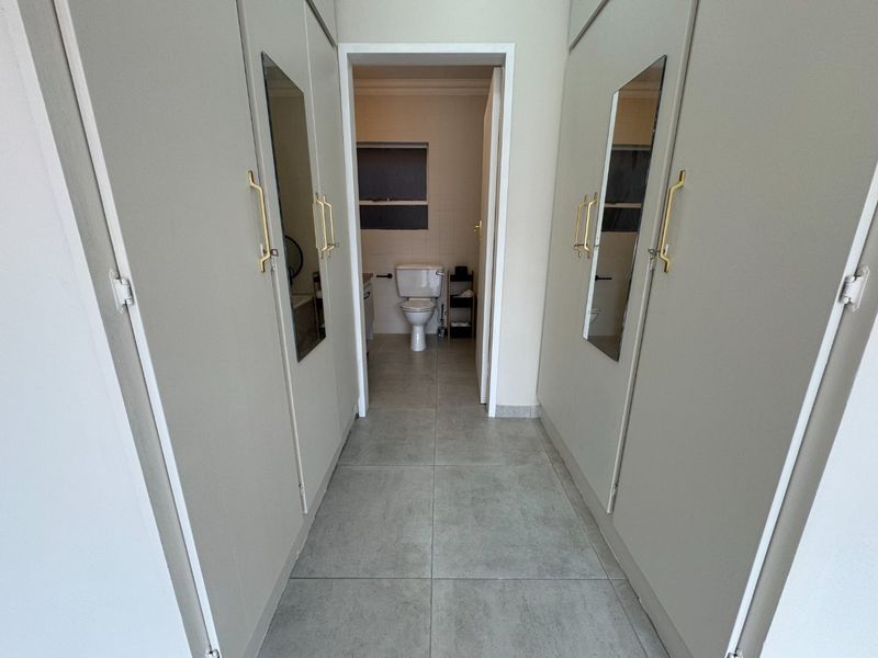 A clean hallway featuring floor-to-ceiling built-in cupboards with mirrored panels and brass hardware, leading directly into a bathroom.