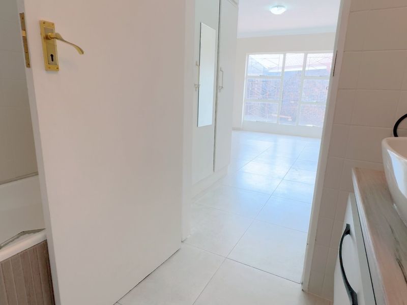 A bright bathroom featuring a built-in bathtub, modern vessel sink on a vanity, and built-in storage cupboards, leading into an adjacent bedroom area.