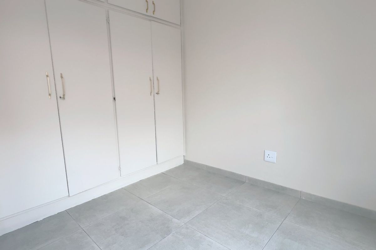 A clean, empty bedroom featuring neutral tiled flooring and ample built-in cupboard storage, providing a versatile space ready for personalization.