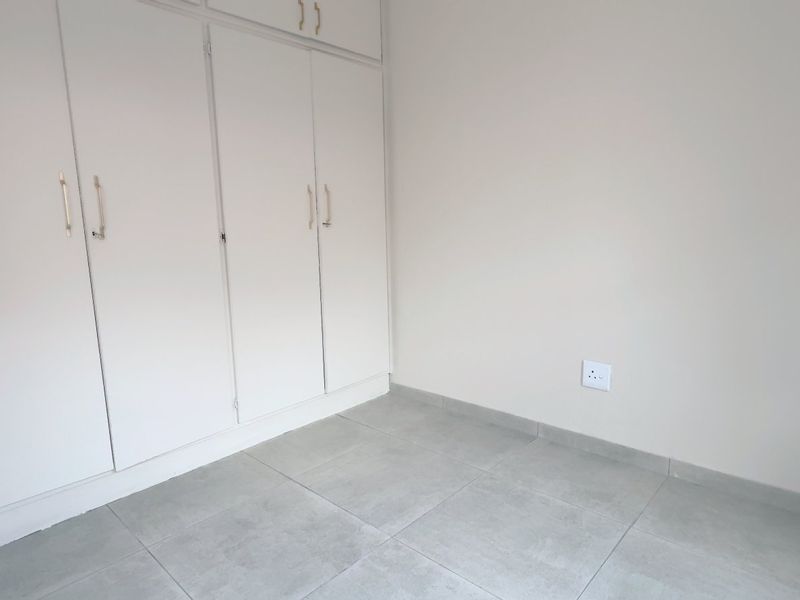 A clean, empty bedroom featuring neutral tiled flooring and ample built-in cupboard storage, providing a versatile space ready for personalization.