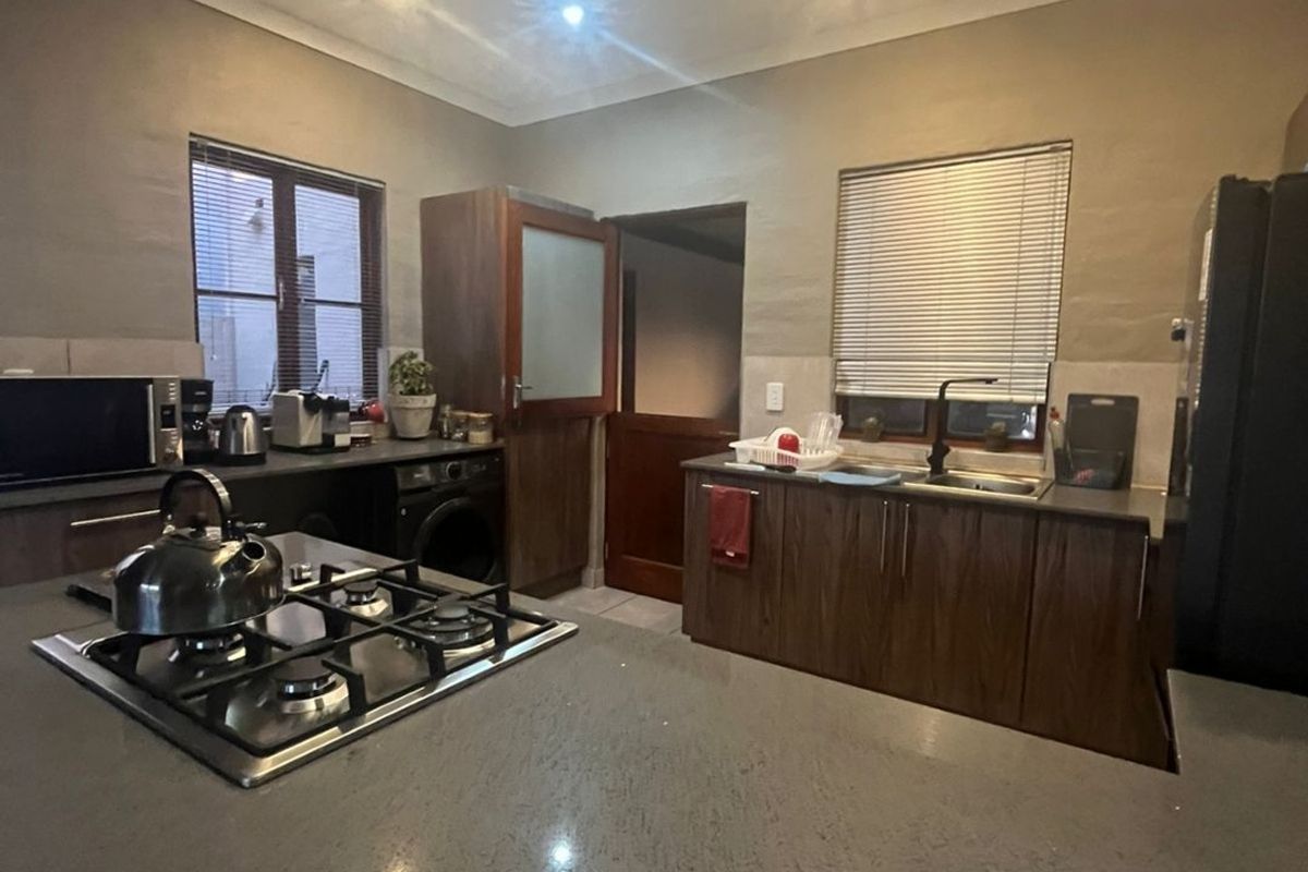 A functional kitchen featuring dark wood cabinetry, stone countertops, a central gas hob, and recessed ceiling lighting.
