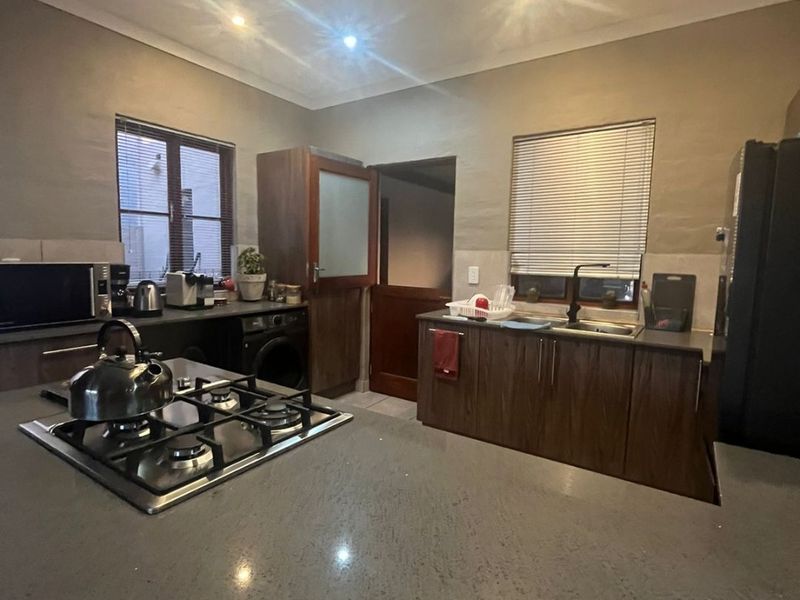 A functional kitchen featuring dark wood cabinetry, stone countertops, a central gas hob, and recessed ceiling lighting.