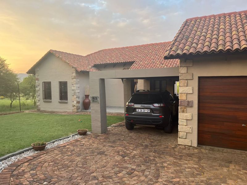 Front elevation of a house featuring terracotta roof tiles, stone cladding accents, a paved driveway, and a covered carport area.