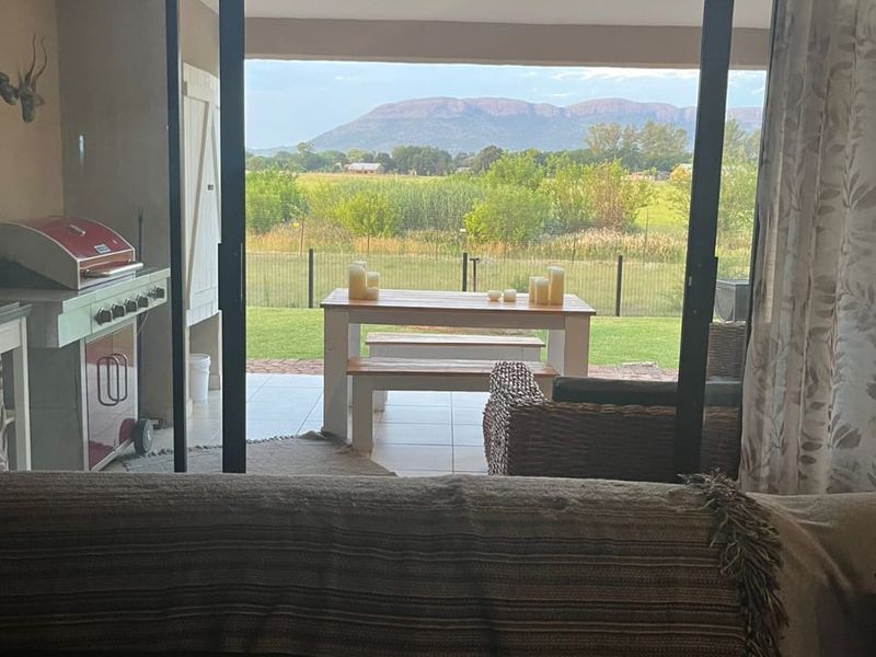 A covered patio area featuring tiled flooring and sliding glass doors, offering scenic views of the surrounding landscape and mountains.