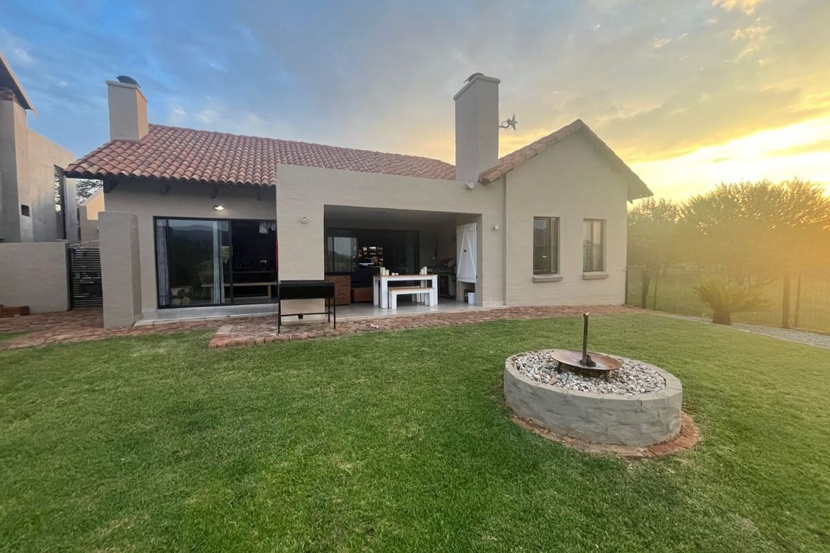 Rear view of the house featuring a covered patio, a built-in fire pit, and a well-maintained garden at sunset.