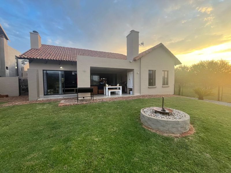 Rear view of the house featuring a covered patio, a built-in fire pit, and a well-maintained garden at sunset.