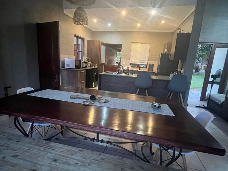 Open-plan living and dining area featuring a kitchen island, tiled flooring, and exposed beam ceilings with modern pendant lighting.