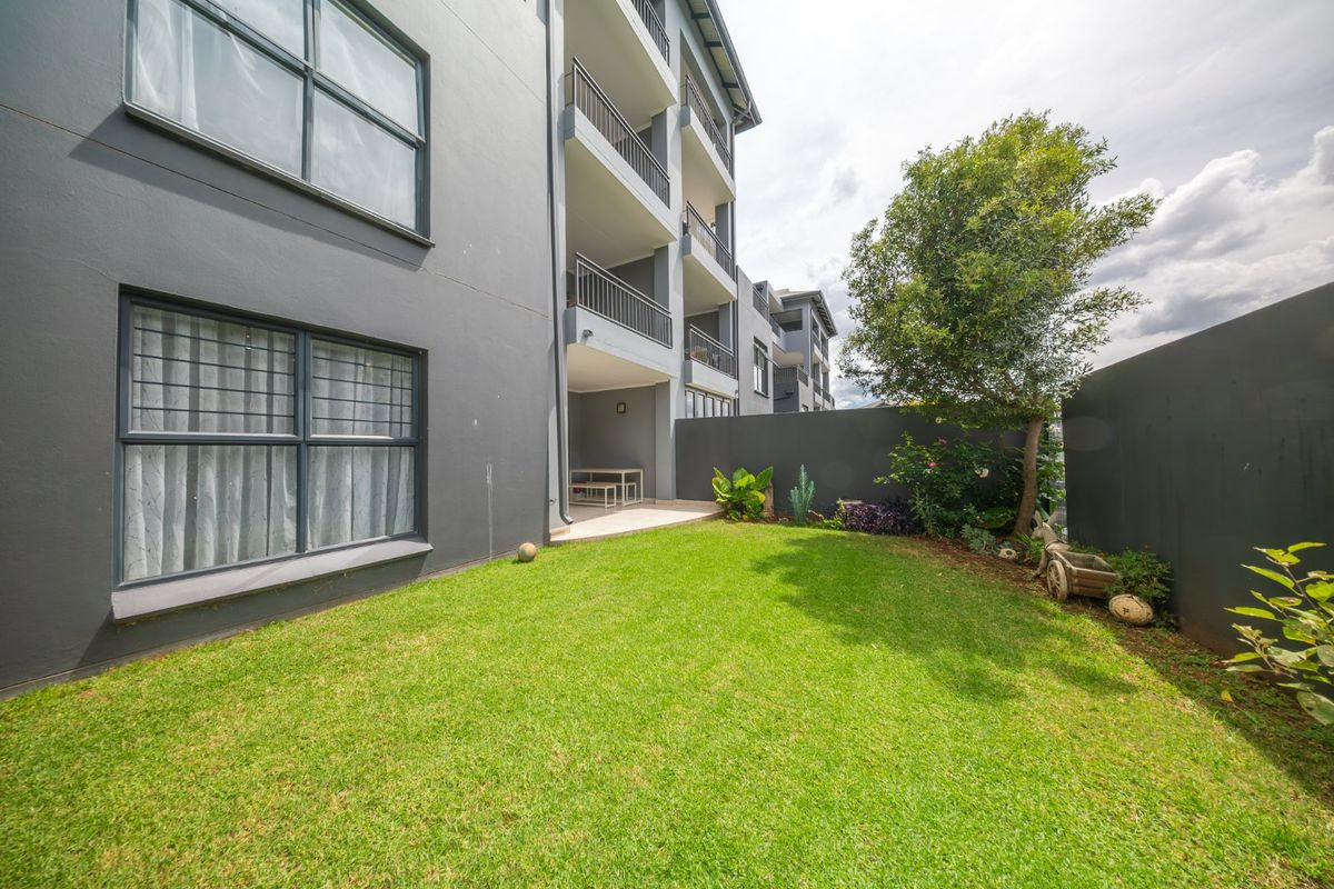 A private rear garden featuring a manicured lawn, boundary wall, and a covered patio area attached to the townhouse structure.