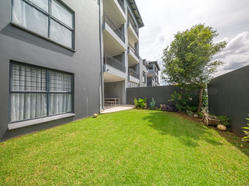 A private rear garden featuring a manicured lawn, boundary wall, and a covered patio area attached to the townhouse structure.