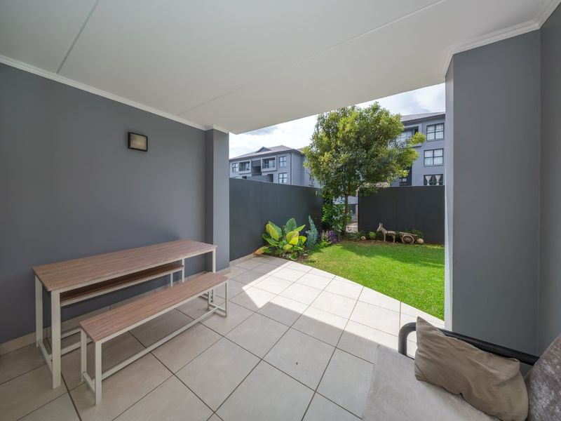 A covered patio area featuring tiled flooring and a wall-mounted light, overlooking a private garden space with a boundary wall.