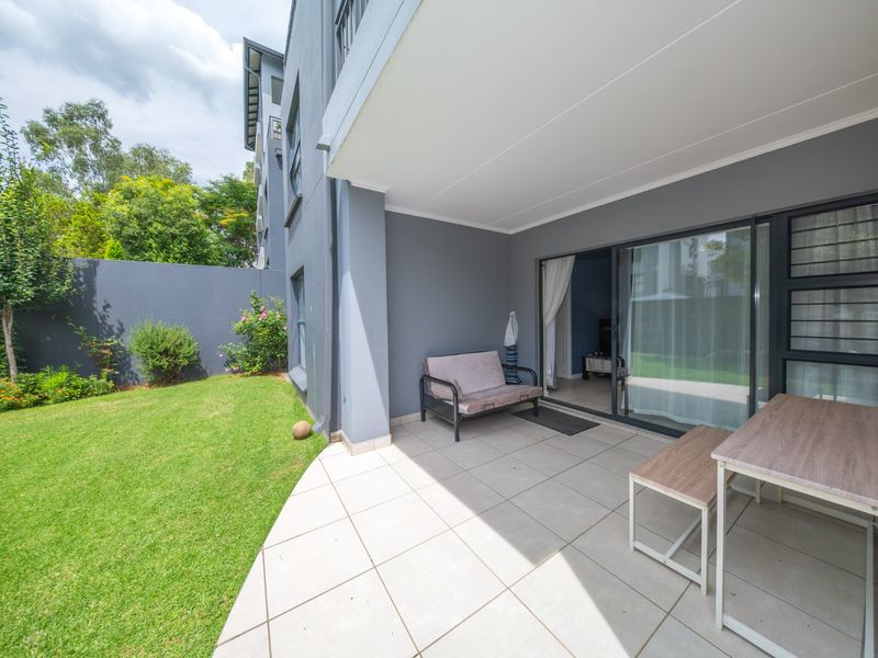 A covered patio area with tiled flooring, providing direct access to the garden through large sliding glass doors.