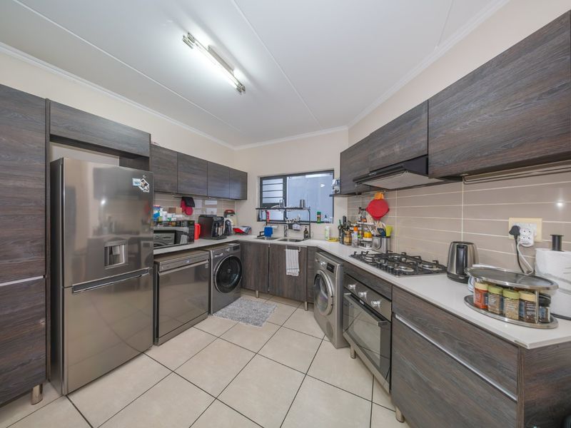 A functional kitchen featuring dark wood-look cabinetry, a gas hob, built-in oven, extractor fan, and tiled flooring with integrated laundry appliance space.