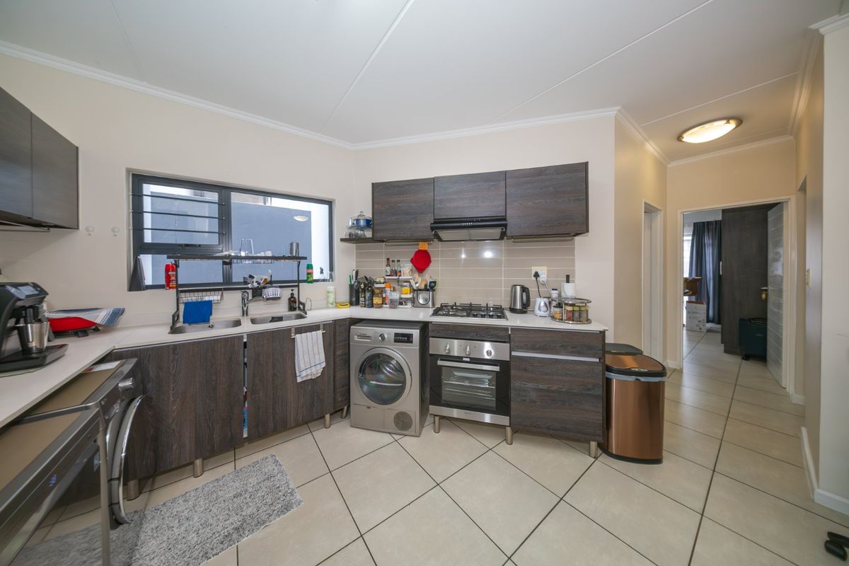 A functional kitchen featuring dark wood-look cabinetry, a gas hob, built-in oven, extractor fan, and tiled flooring with a double sink.