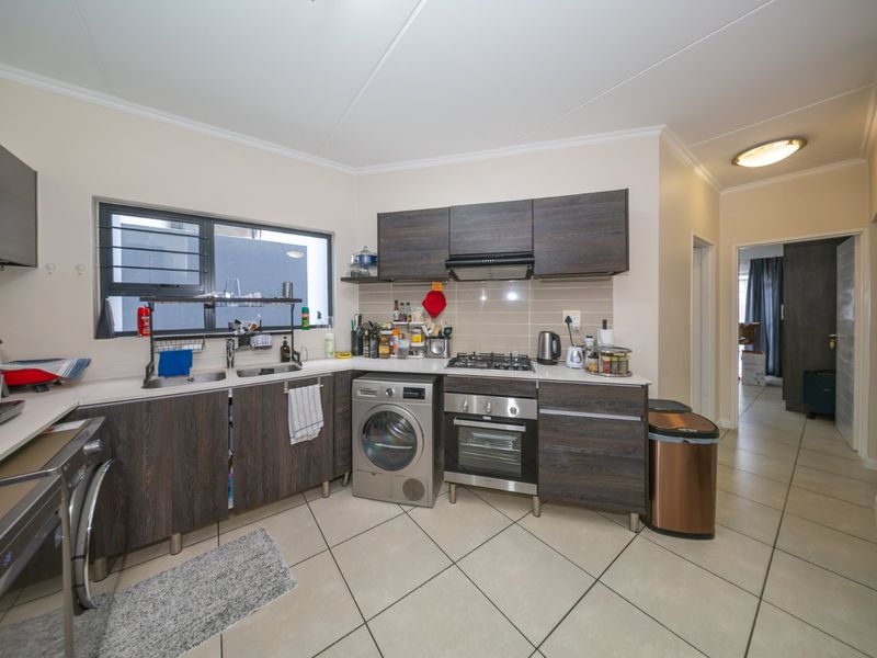 A functional kitchen featuring dark wood-look cabinetry, a gas hob, built-in oven, extractor fan, and tiled flooring with a double sink.