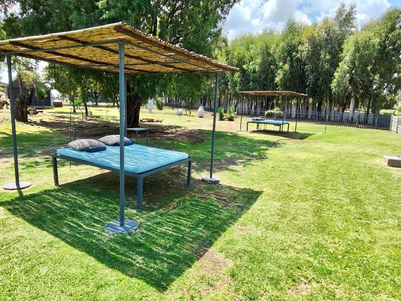 A spacious, well-maintained garden area featuring established trees, manicured lawn, and shaded outdoor relaxation structures enclosed by a precast concrete boundary wall.