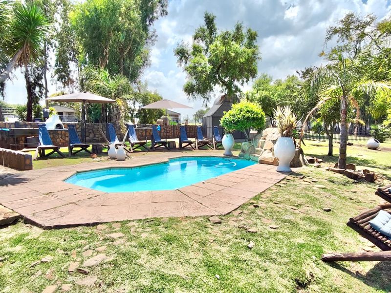Outdoor pool area featuring a swimming pool, stone paving, and a built-in braai, set within a landscaped garden environment.