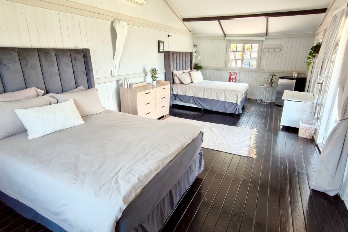 Spacious bedroom featuring timber wall paneling, exposed ceiling beams, dark timber flooring, and a split-system air conditioner.