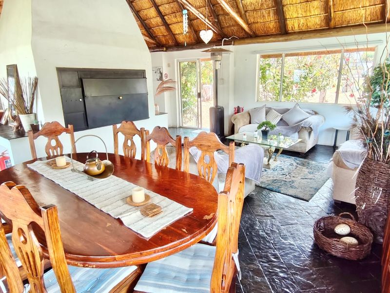 Spacious open-plan living and dining area featuring a traditional thatched roof, exposed timber rafters, and a large built-in fireplace with direct garden access.