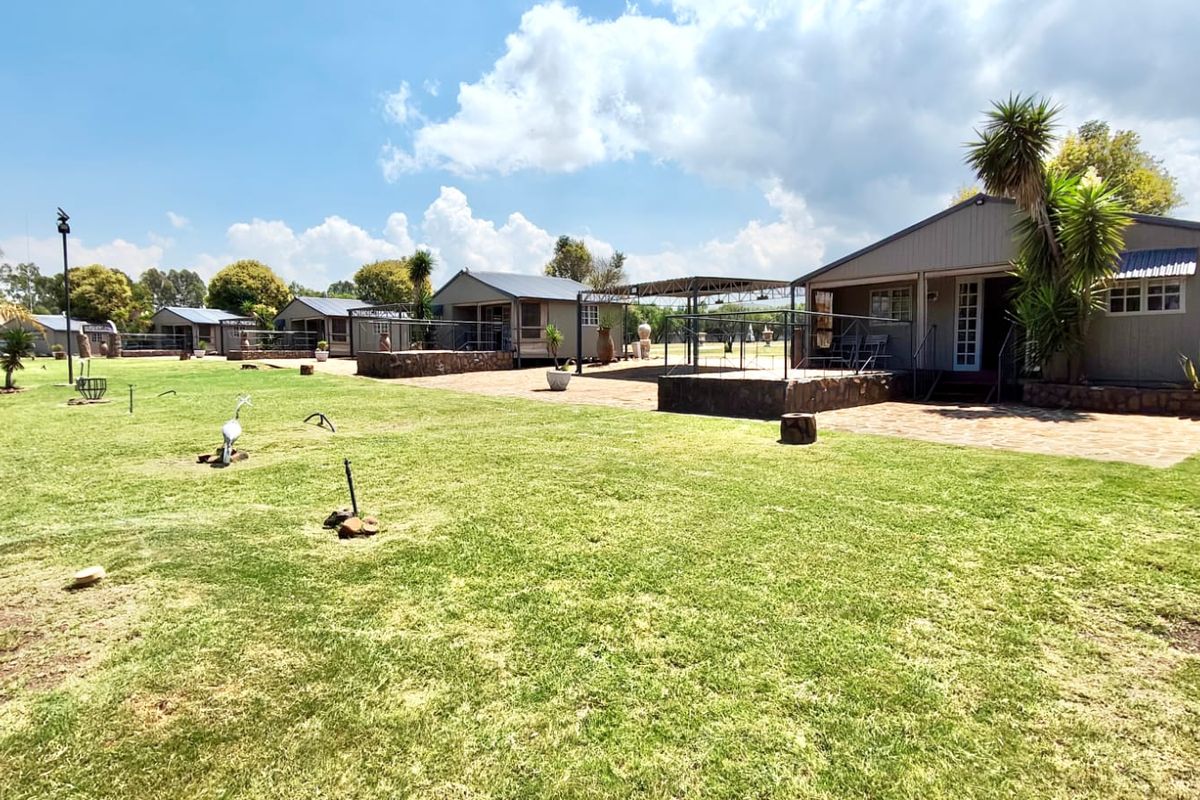 A view of the rear exterior of the farm property, featuring multiple detached units with stone-clad patios and well-maintained lawn areas.