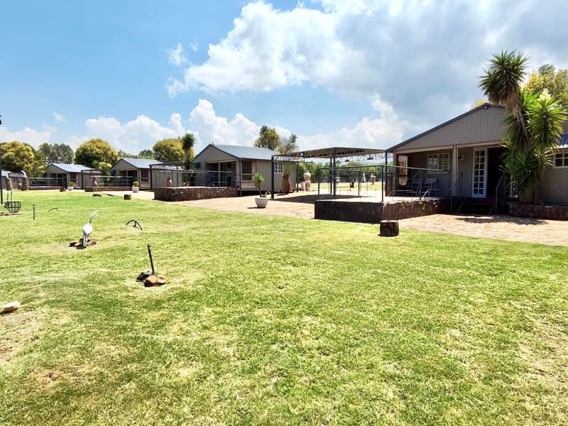 A view of the rear exterior of the farm property, featuring multiple detached units with stone-clad patios and well-maintained lawn areas.