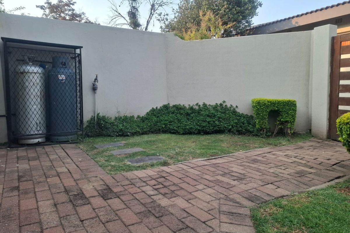 A private rear courtyard area featuring a paved walkway, perimeter wall, and a secure gas cylinder storage cage.