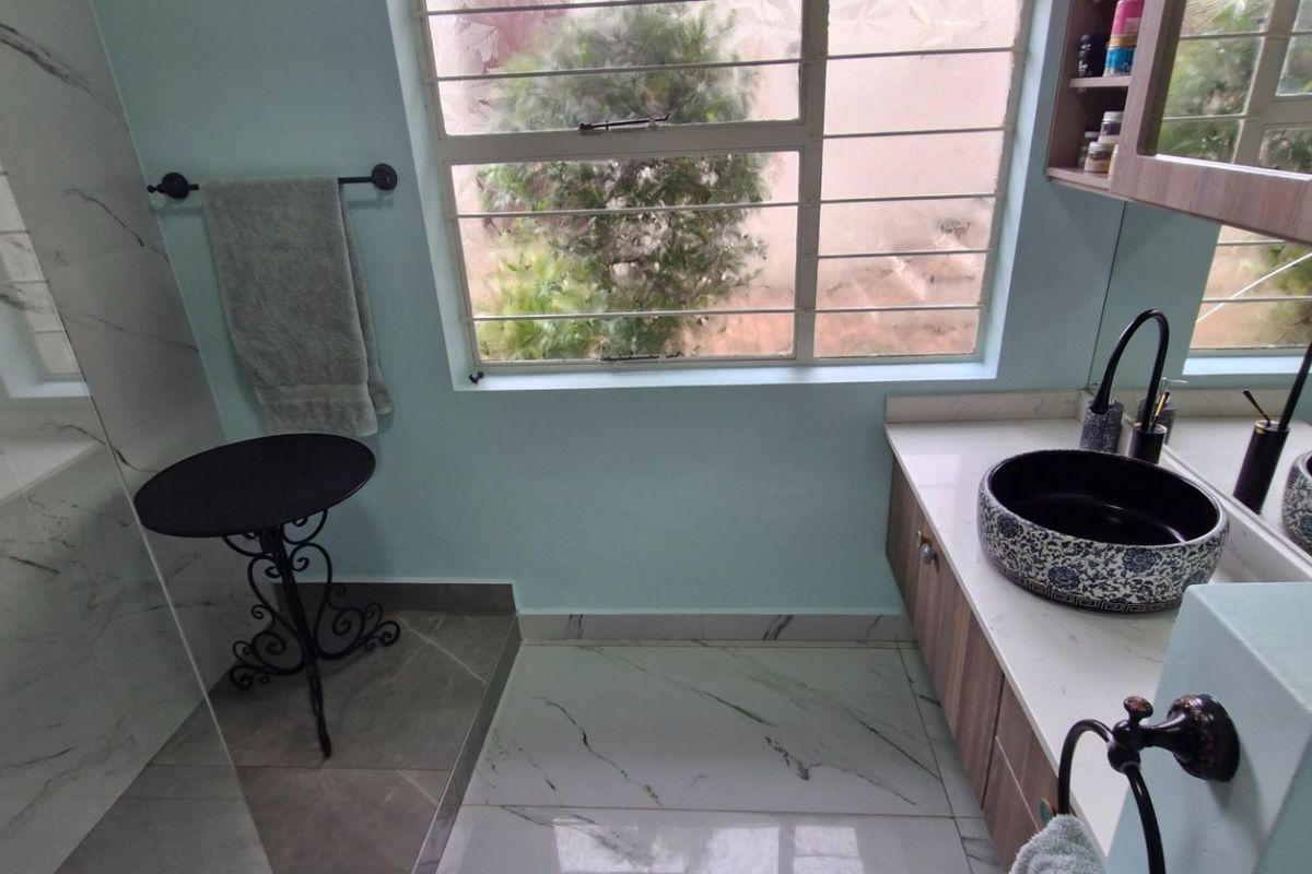 A modern bathroom featuring a decorative vessel sink, marble-look floor tiles, and a wall-mounted vanity cabinet with integrated storage.