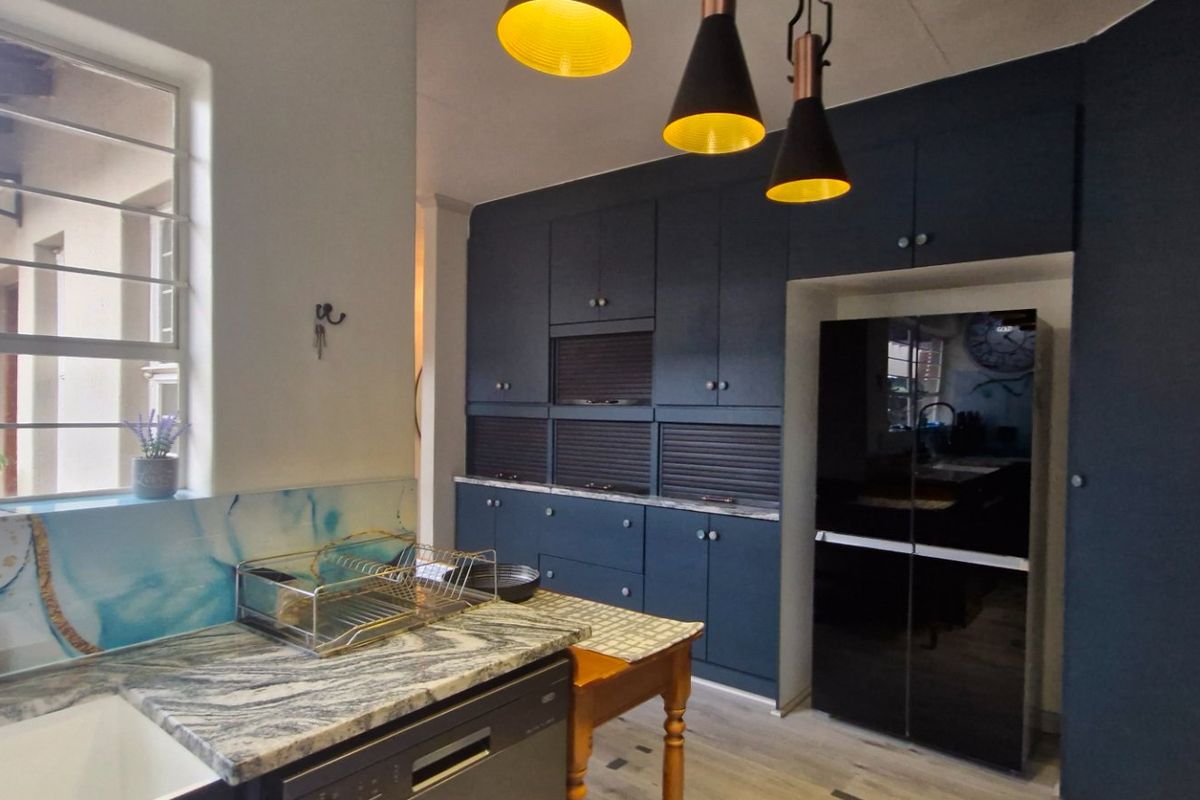 Modern kitchen featuring dark blue cabinetry, stone countertops, integrated appliances, and stylish pendant lighting, offering a contemporary and functional workspace.