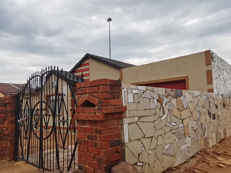 Front elevation of a residential property featuring a brick boundary wall with decorative mosaic tiling and a secure wrought iron entrance gate.