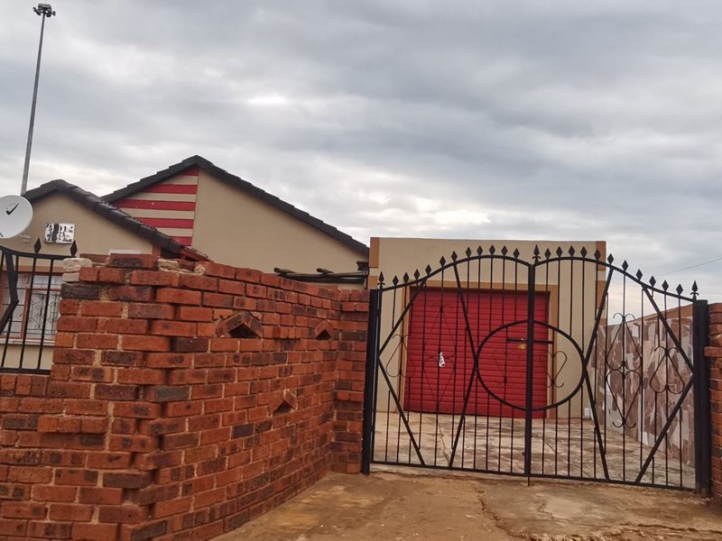 Front exterior view of the property featuring a brick boundary wall, wrought iron gate, and a garage with a red door.
