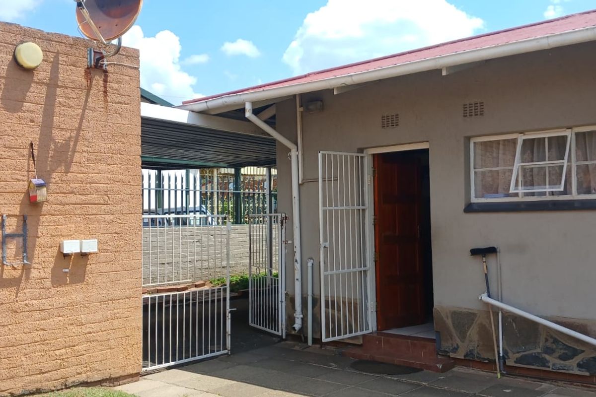 Rear exterior view of the property featuring a paved patio area, security gates, and a solar water heating system.
