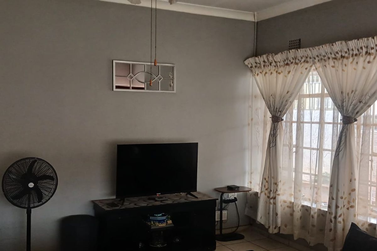 A living room featuring tiled flooring, security bars on the windows, and decorative coving, providing a functional and neutral space.