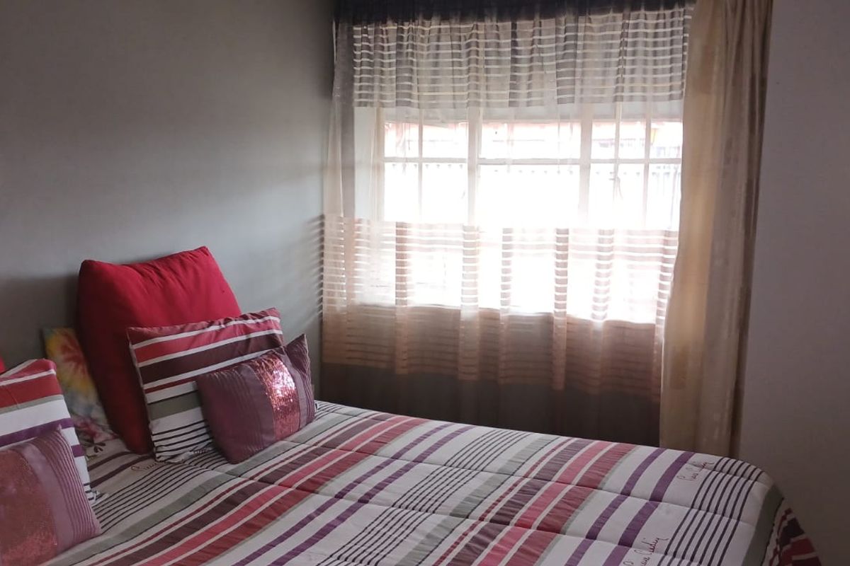A standard bedroom featuring a built-in wardrobe and a window with security bars, providing natural light and functional storage space.