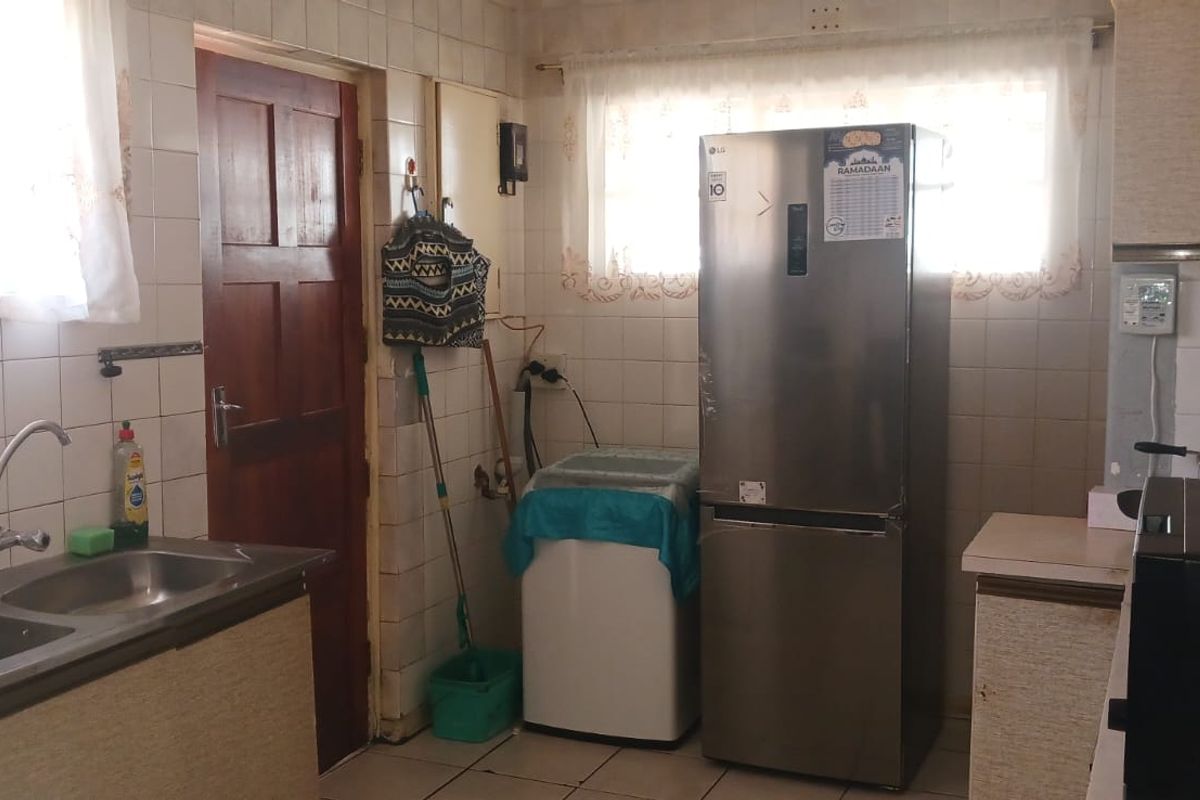 A functional kitchen featuring tiled walls, double stainless steel sink, and fitted cabinetry, offering a dated aesthetic with potential for modernization.