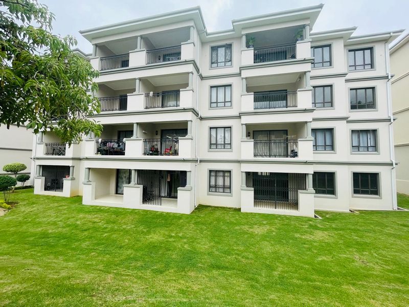 Rear elevation of a multi-story apartment complex featuring private balconies, sliding glass doors, security fixtures, and a well-maintained communal lawn area.