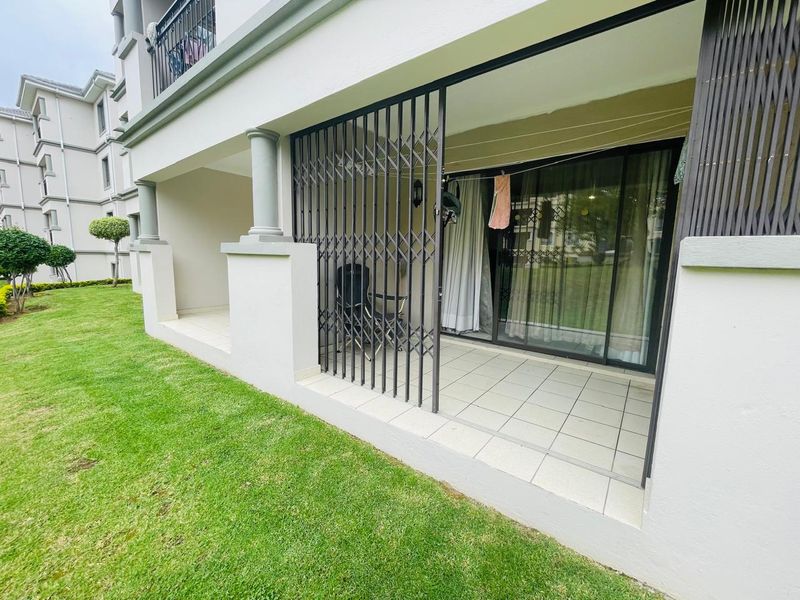 A ground floor patio featuring tiled flooring, concrete columns, and a security gate, providing direct access to the apartment's exterior garden area.