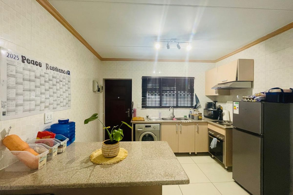 A functional kitchen featuring built-in cabinetry, granite countertops, a stainless steel sink, and integrated oven with extractor fan, finished with tiled walls and flooring.