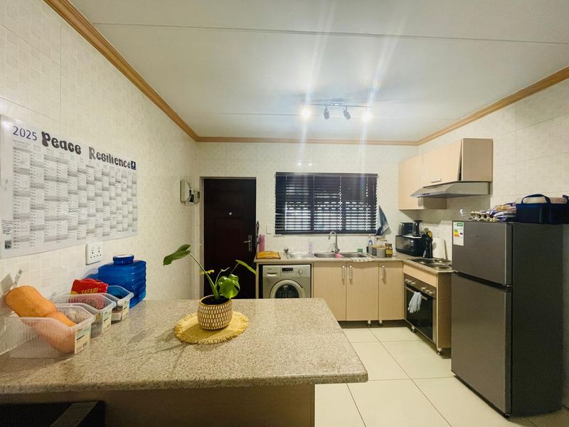 A functional kitchen featuring built-in cabinetry, granite countertops, a stainless steel sink, and integrated oven with extractor fan, finished with tiled walls and flooring.