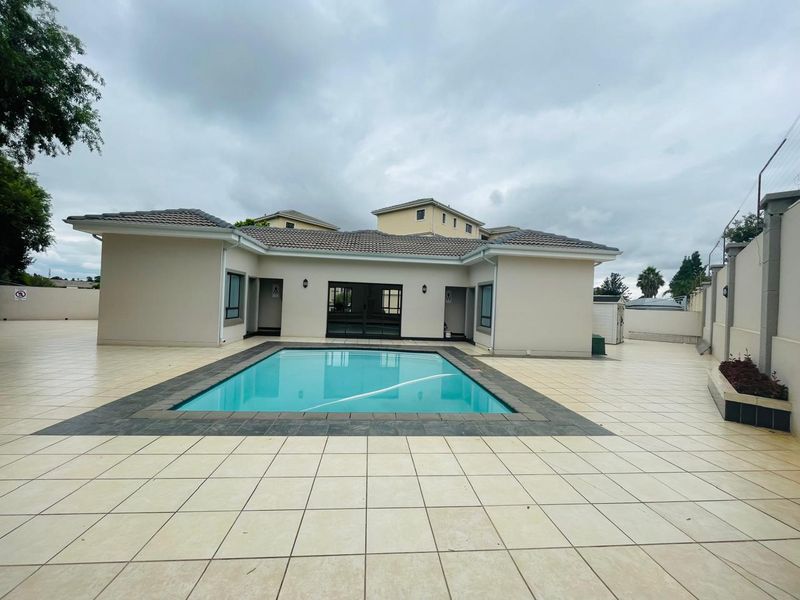 A well-maintained outdoor pool area featuring a tiled patio, perimeter wall, and direct access to the main building via sliding doors.