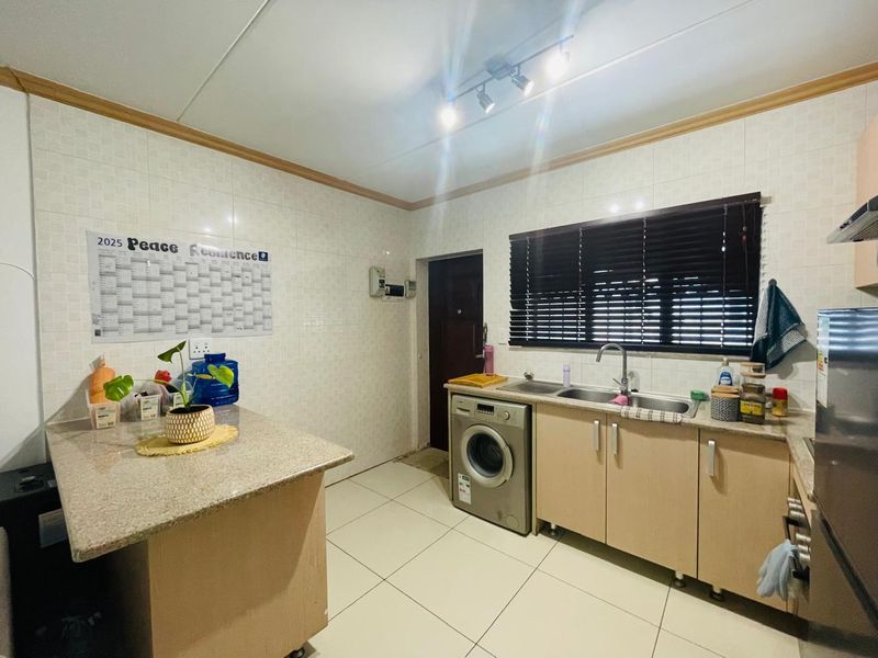 A functional kitchen featuring granite countertops, built-in cabinetry, tiled walls and flooring, and a stainless steel sink with integrated laundry appliance space.