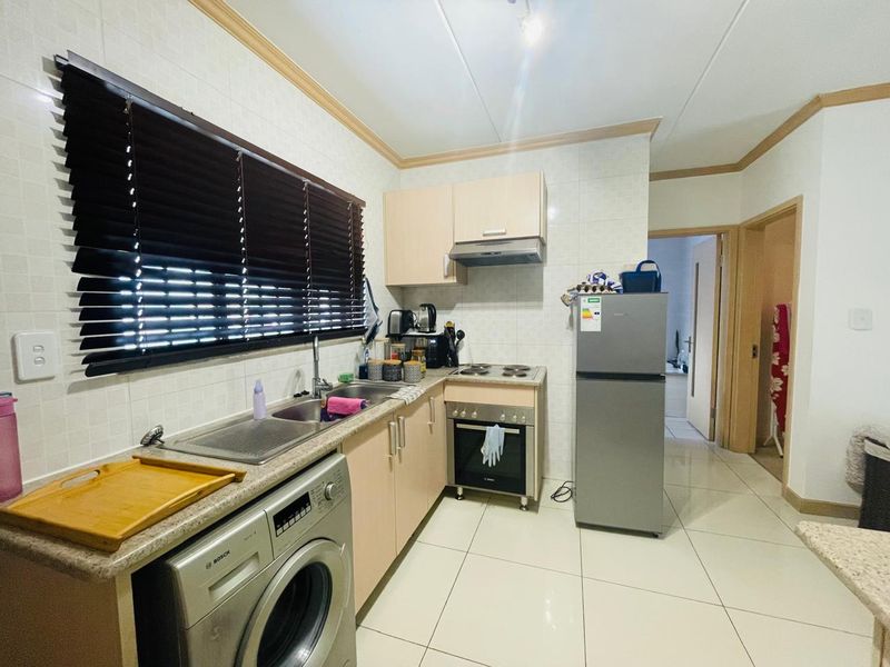 A functional kitchen featuring built-in cabinetry, tiled flooring, a stainless steel sink, and integrated cooking appliances with a tiled backsplash.