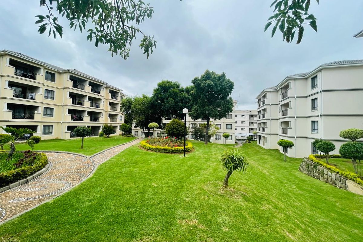 A well-maintained communal garden area featuring manicured lawns, paved pathways, and established landscaping between apartment blocks.
