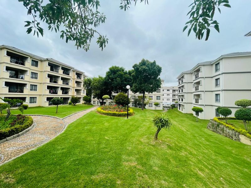 A well-maintained communal garden area featuring manicured lawns, paved pathways, and established landscaping between apartment blocks.