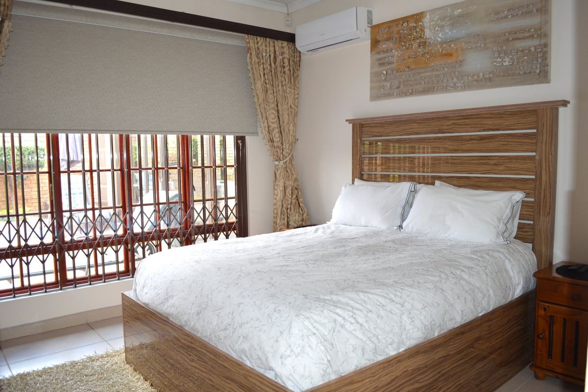 A well-maintained bedroom featuring tiled flooring, a wall-mounted air conditioning unit, and secure window treatments.
