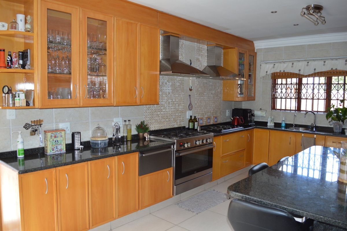 Spacious kitchen featuring warm wooden cabinetry, granite countertops, a gas stove with dual extractor fans, and a tiled backsplash with integrated lighting.