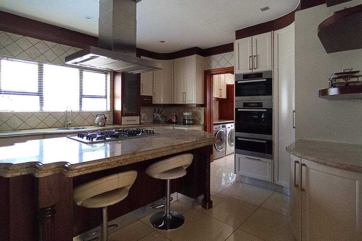 Spacious kitchen featuring a large island with gas hob, granite countertops, built-in appliances, and ample cabinetry, with an adjacent laundry area visible.